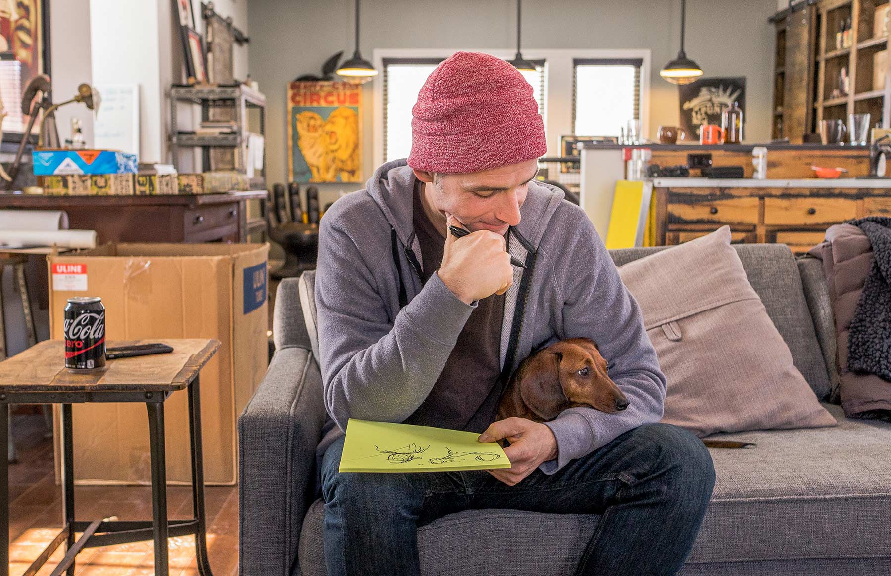 A-man-sketching-on-a-notepad-with-a-Dachshund-on-his-lap