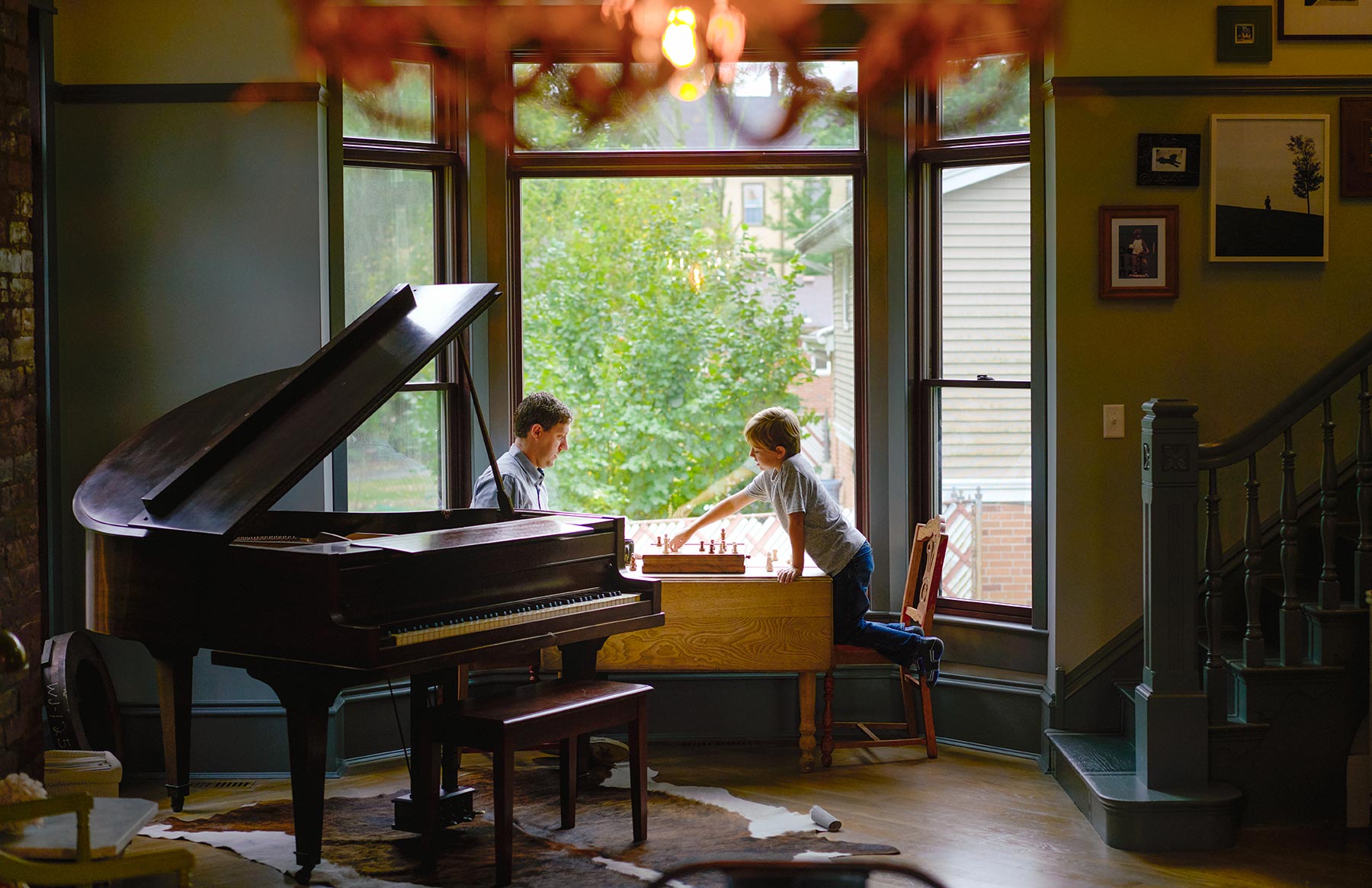 A-father-and-son-playing-chess-between-a-grand-piano-and-a-large-window-in-the-living-room-of-their-house