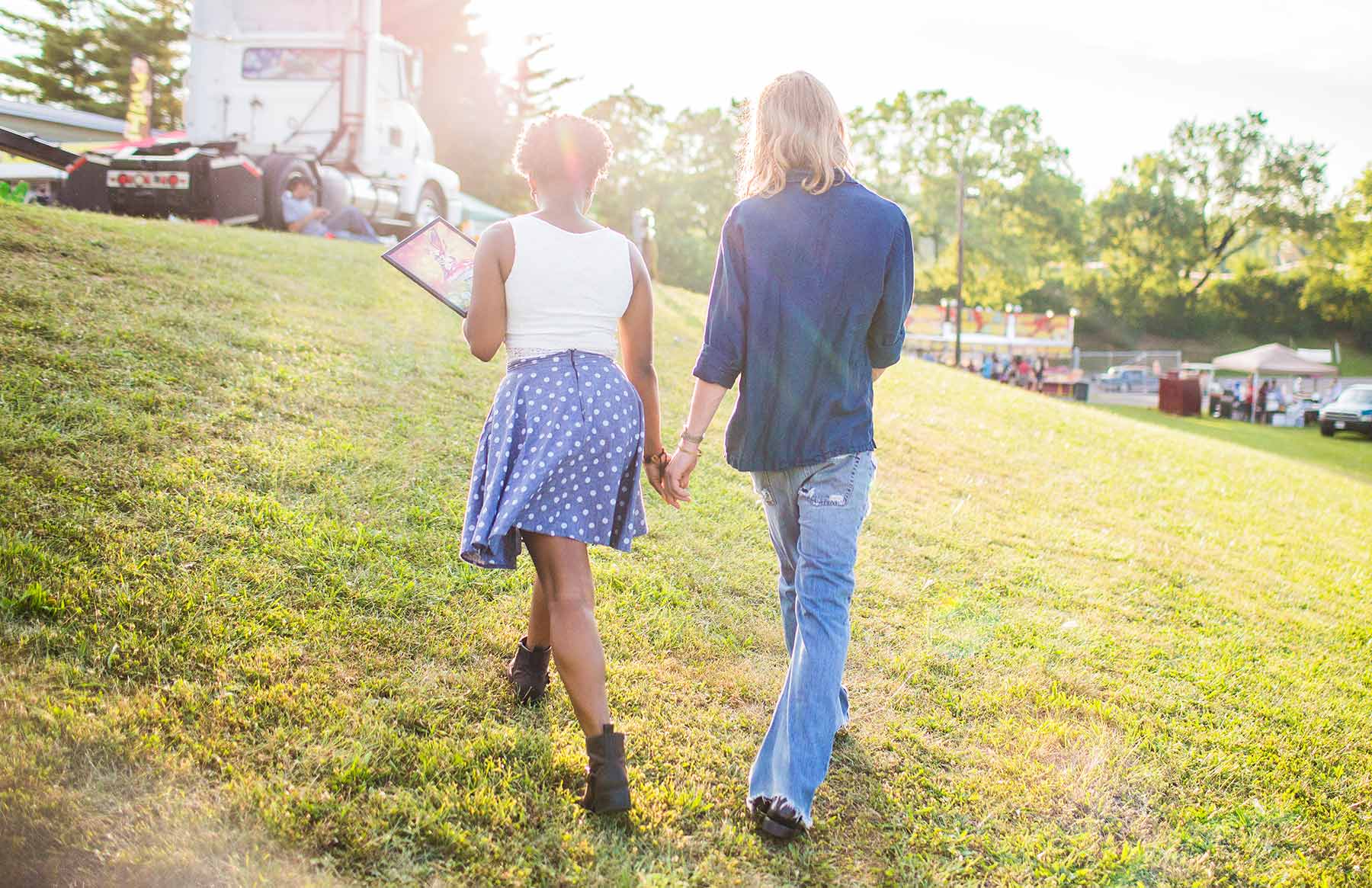 A-young-couple-holding-hands-while-walking-up-a-grassy-hill-on-a-sunny-day